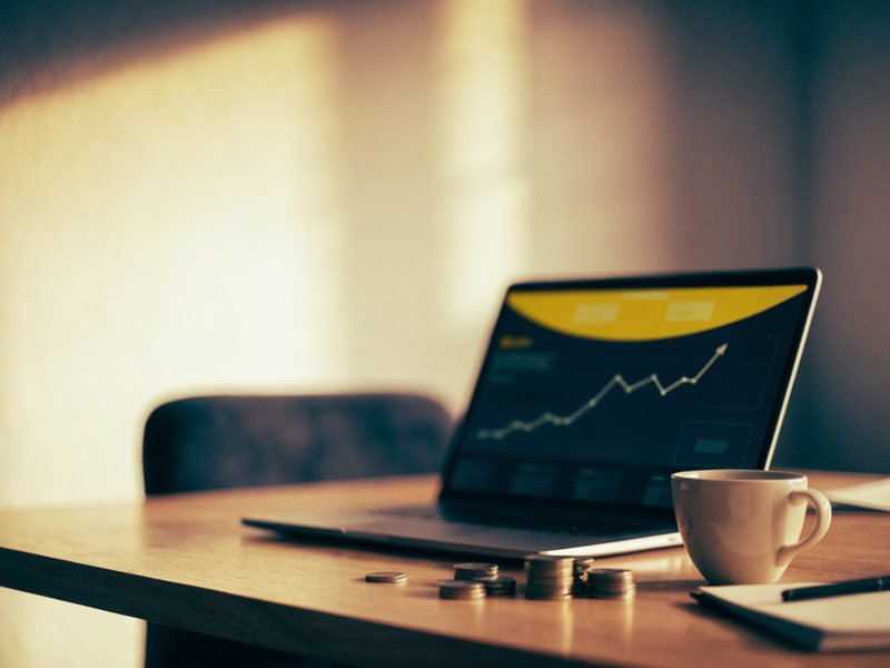 Laptop mit steigender Werbe-Statistik und Münzen auf dem Schreibtisch