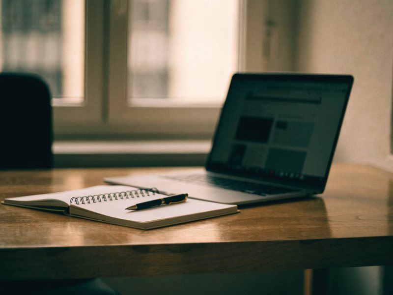 Notizbuch mit Stift neben Laptop mit Website-Textblöcken auf einem Schreibtisch