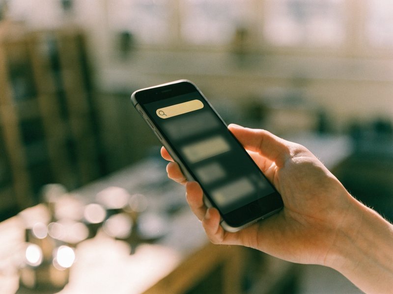Hand mit Smartphone und Suchleiste – nach lokalen Betrieben googeln